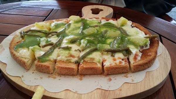 Sliced flatbread with melted cheese, green beans and pesto on wooden board