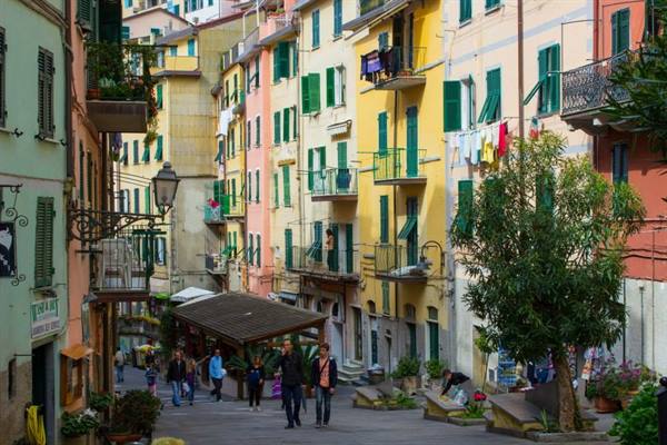 Colorful houses with green shutters in Vernazza, tourists walk down the street