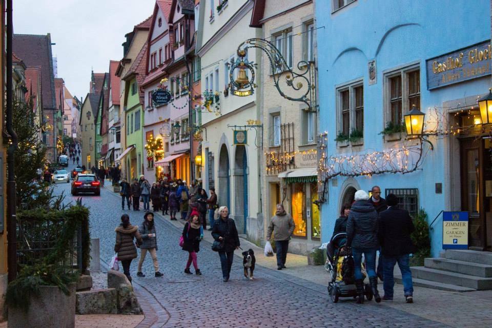 Turisti passeggiano sul selciato di Rothenburg tra case colorate e insegne di Natale