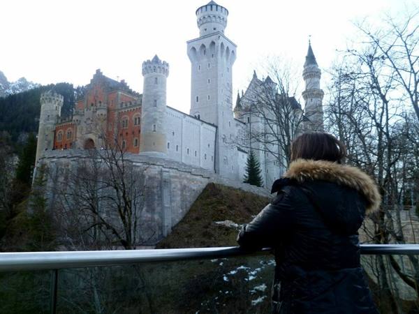 Tourist in fur-hooded coat admires Neuschwanstein Castle among bare trees