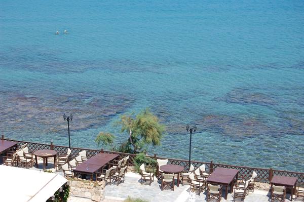 Empty wooden tables and chairs on terrace above clear turquoise sea
