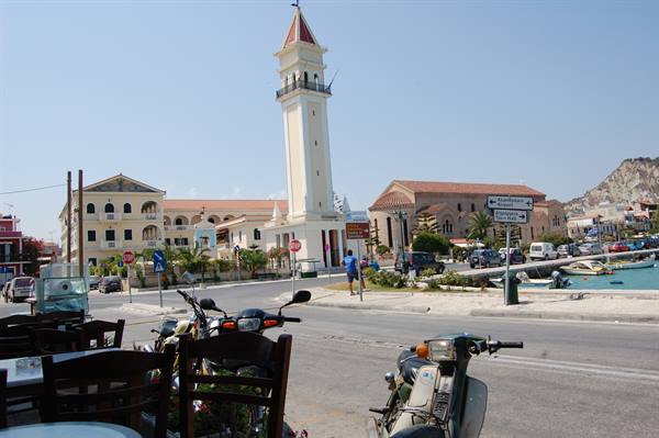 Scooters and chairs in foreground, white bell tower and harbor, Zakynthos