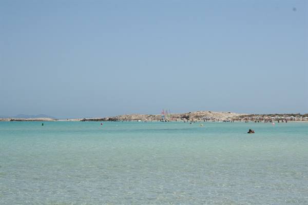 Clear turquoise water, swimmers and sandy beach with umbrellas under blue sky