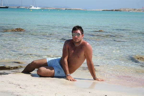 Man in blue swim shorts lying on shallow turquoise water, boats moored offshore