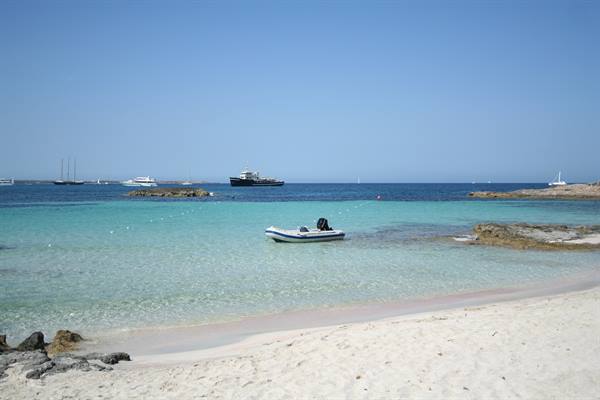Inflatable boat anchored in turquoise bay with pale sand and ships on horizon