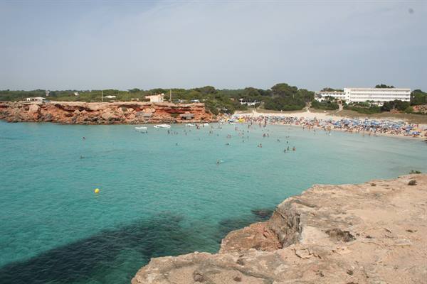 Swimmers in turquoise water between red rocks and sandy beach