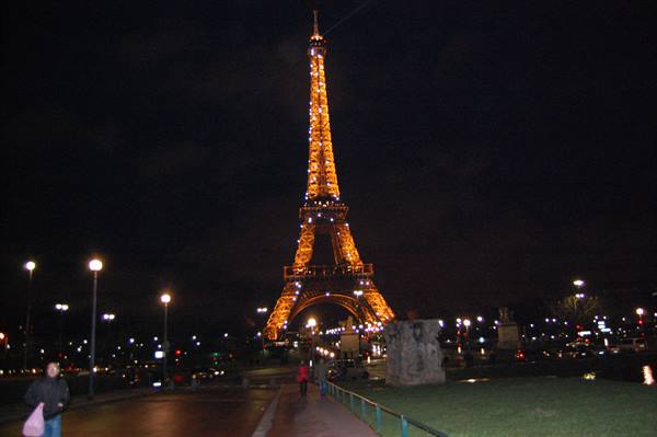 The Eiffel Tower glowing golden at night, people walking on the avenue