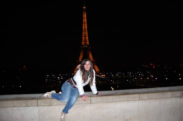 Girl posing on stone ledge in front of the illuminated Eiffel Tower at night
