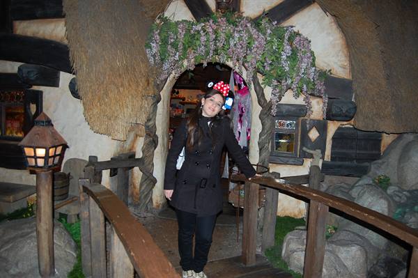 Girl wearing Minnie ears on wooden bridge in front of thatched cottage