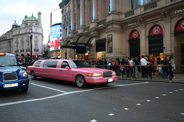 Pink limousine crossing Piccadilly Circus among taxis and crowd