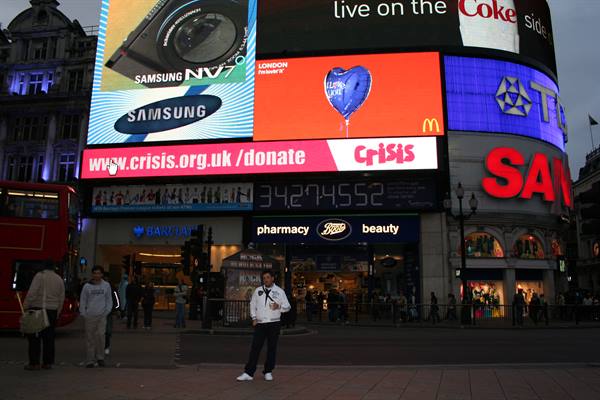 Man poses before the glowing billboards of Piccadilly Circus, London