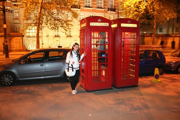 Woman beside London's red telephone boxes lit at night