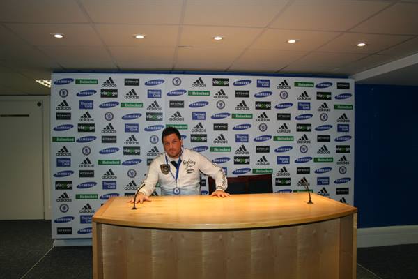 Man with medal at Stamford Bridge press room, wooden desk