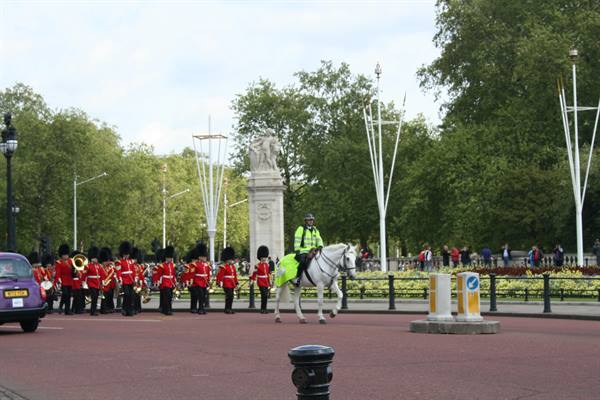 Red-uniformed guards marching past mounted officer on white horse, London