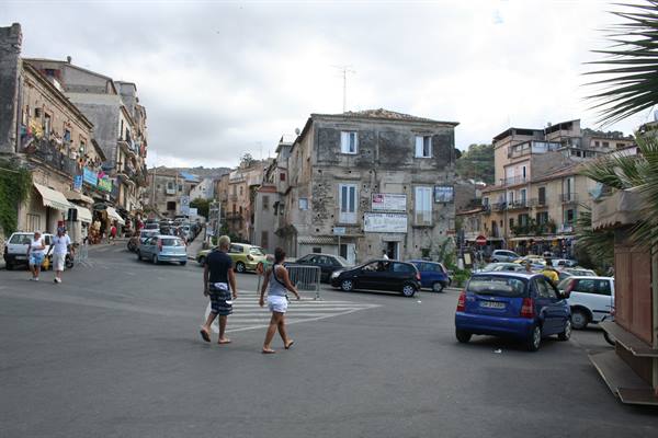 Tourists cross a square with parked cars among old stone buildings