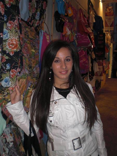 Girl in white jacket smiling among floral clothes and bags in a shop