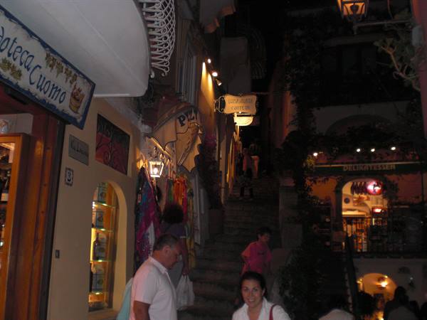 Night staircase with lit shop signs and people walking, likely Positano