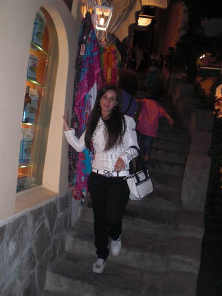 Woman in white jacket and bag walking down stone steps past colorful scarves