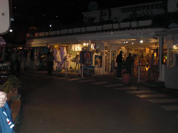 Tourists browsing lit souvenir and clothing shops at night