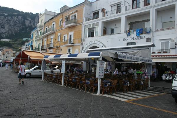 Square with bar gelateria, wicker chairs under white and blue awnings, colorful buildings