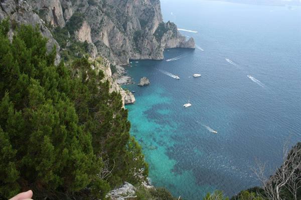 Limestone cliffs of Capri above turquoise waters with boats sailing by