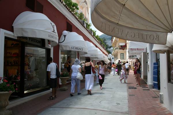 Tourists stroll past luxury boutiques under white awnings in Capri