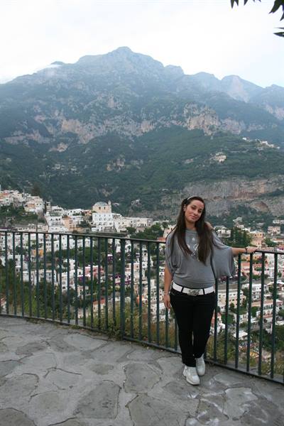 Woman leaning on an iron railing in front of a hillside village