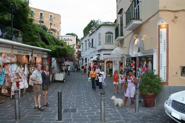 Tourists stroll past souvenir shops along a stone-paved lane in Capri
