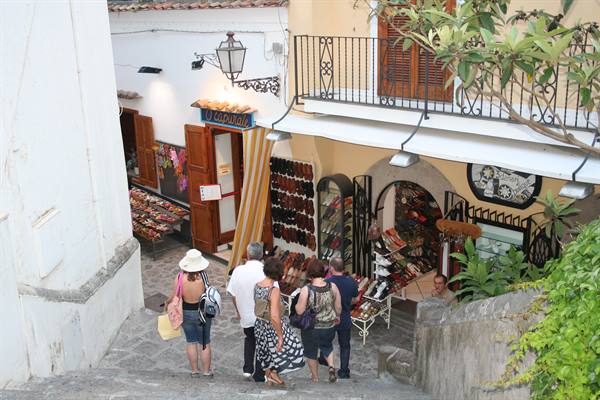 Tourists walk down steps past leather sandal shops and ceramics