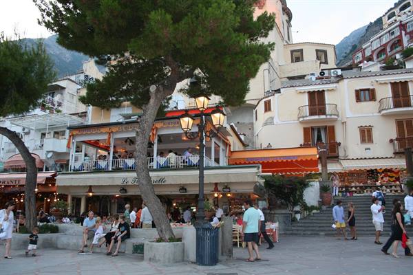 Square with pine trees, orange-awning cafés and strolling tourists in Positano