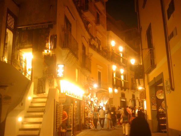 Night alley lit by street lamps, shops and tobacco sign, tourists strolling