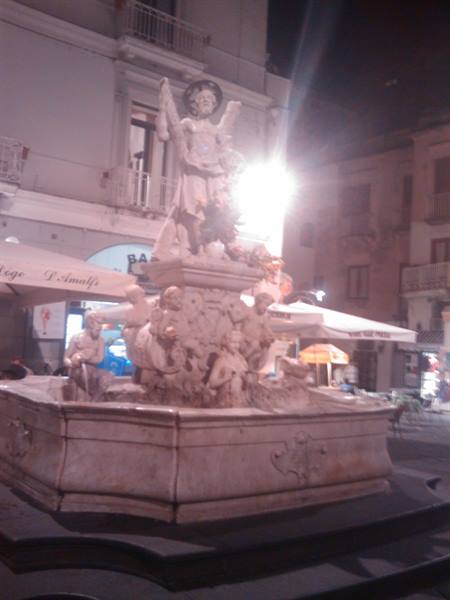Baroque marble fountain with central statue lit at night in Amalfi square