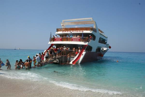 Tourists board a white and red ferry beached on the shore, turquoise sea