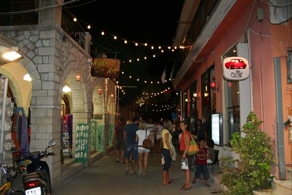 Tourists stroll under colorful string lights in Laganas pedestrian street at night