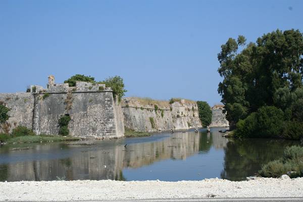 Stone fortress bastion walls reflect in the water moat under clear blue sky