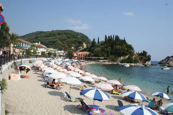 Crowded Parga beach: sun umbrellas, sand, swimmers and pine trees by the sea