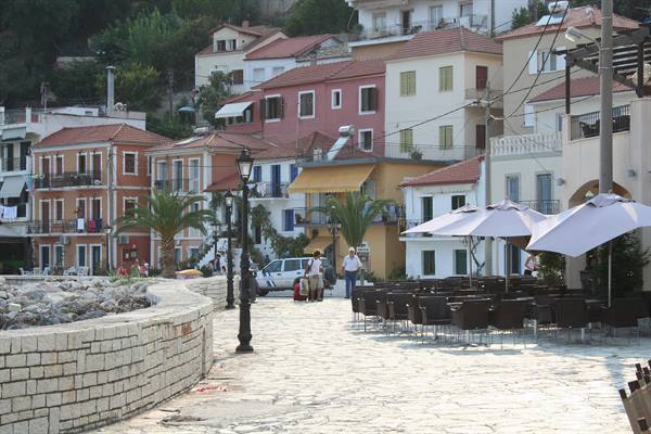 Stone promenade with umbrella-shaded café tables in front of Parga's colorful houses