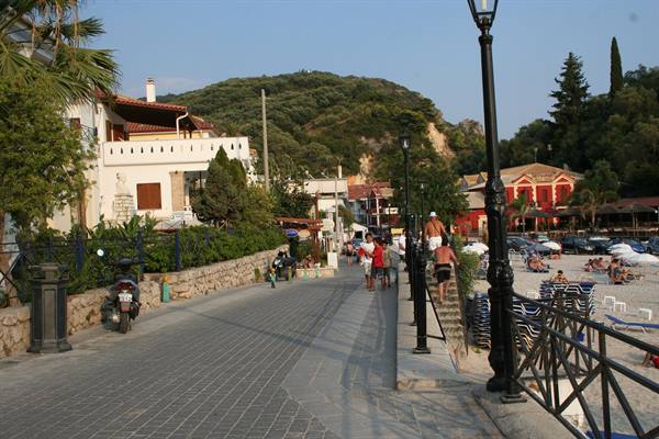 stone-paved seafront promenade with lampposts, tourists walking to the sandy beach