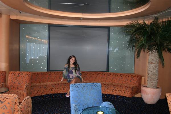 Girl sitting on orange sofa in a lounge with palm tree and blue armchair