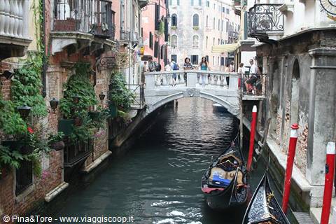 Tourists on a stone bridge over a canal with gondolas in Venice