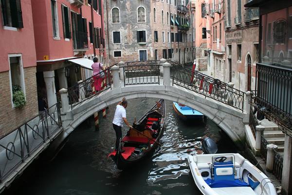 Gondolier passing under a stone bridge in Venice, old buildings and moored boats