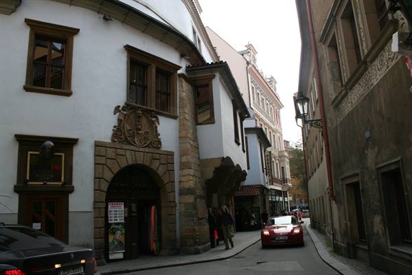 Narrow street with historic buildings and stone portal, parked cars, Prague