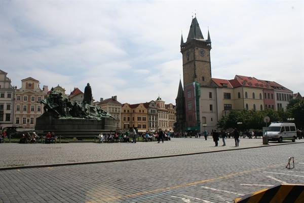 Tourists sitting around Jan Hus monument and old town hall tower, Prague