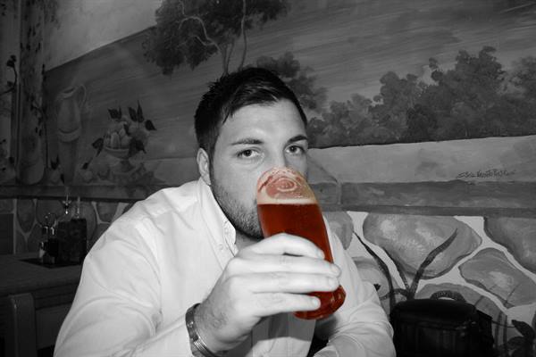 Man in white shirt drinks red beer in front of a black and white mural