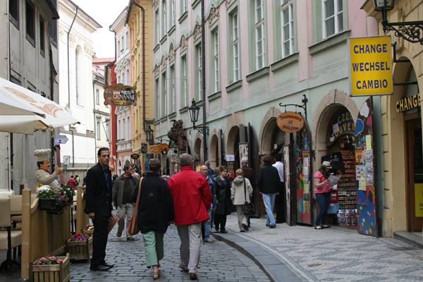 Tourists walking on cobblestone lane past colorful buildings and souvenir shops