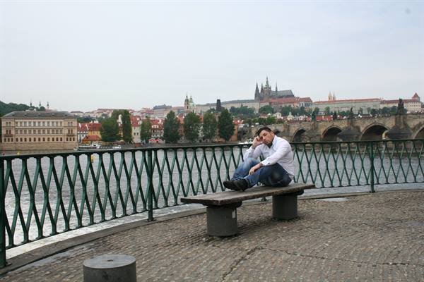 Young man on a wooden bench by the Vltava river, Prague Castle in the background