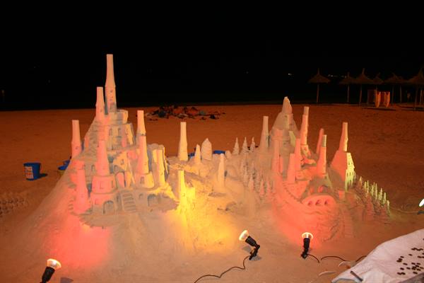 Sand castle lit at night by colored spotlights on the beach