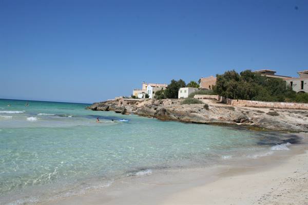 Turquoise water on sandy beach, swimmers near rocky cliffs with white houses