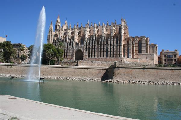 Palma Cathedral in Mallorca, golden stone, lake fountain under blue sky