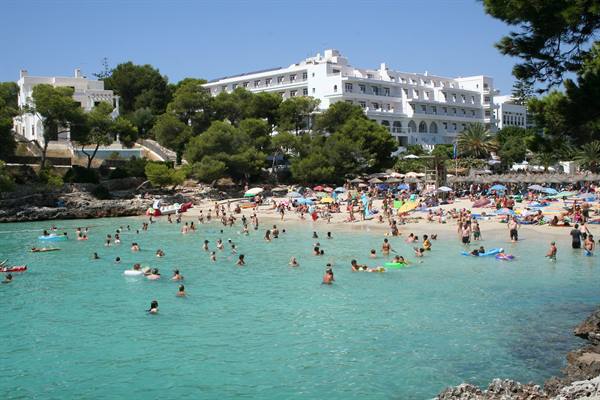 Swimmers in turquoise bay, crowded beach with umbrellas in front of a large white hotel